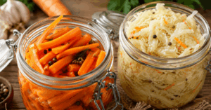 Nahaufnahme von fermentierten Karotten und Sauerkraut in Einmachgläsern auf einem rustikalen Holztisch zur natürlichen Haltbarmachung von Gemüse.